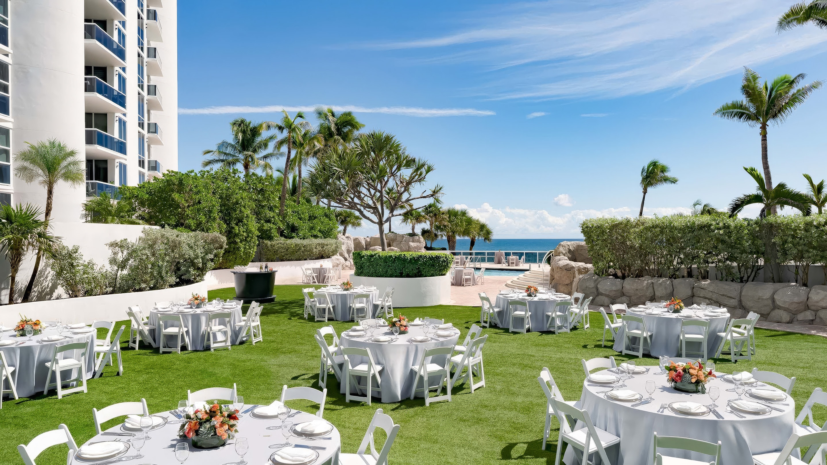 a group of tables and chairs in a grassy area with a pool and trees