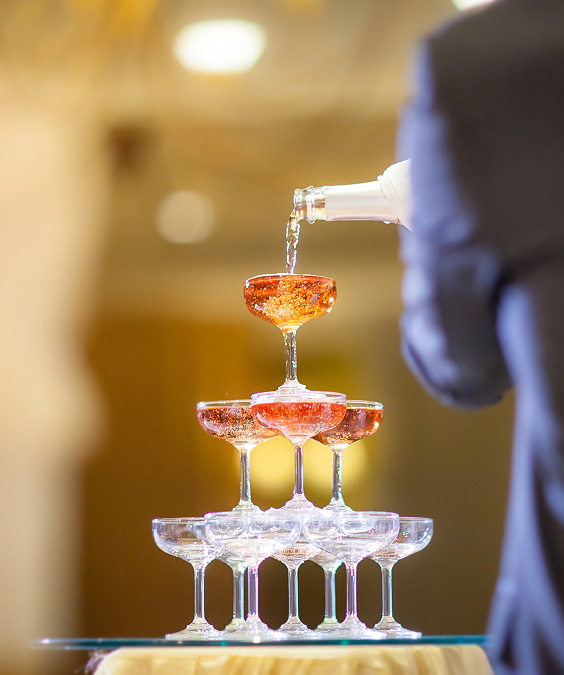 a person pouring liquid into a pyramid of champagne glasses