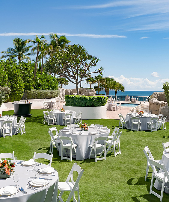 a group of tables and chairs on a lawn with a pool in the background
