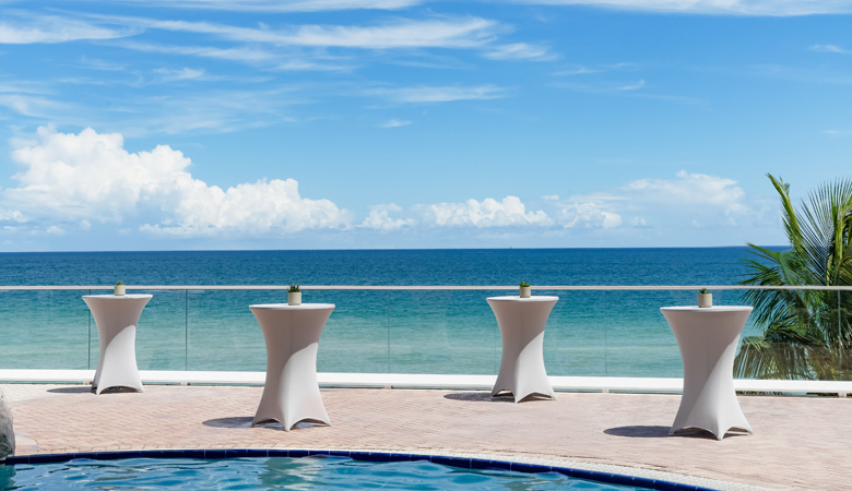 tables on a patio with a pool and water in the background