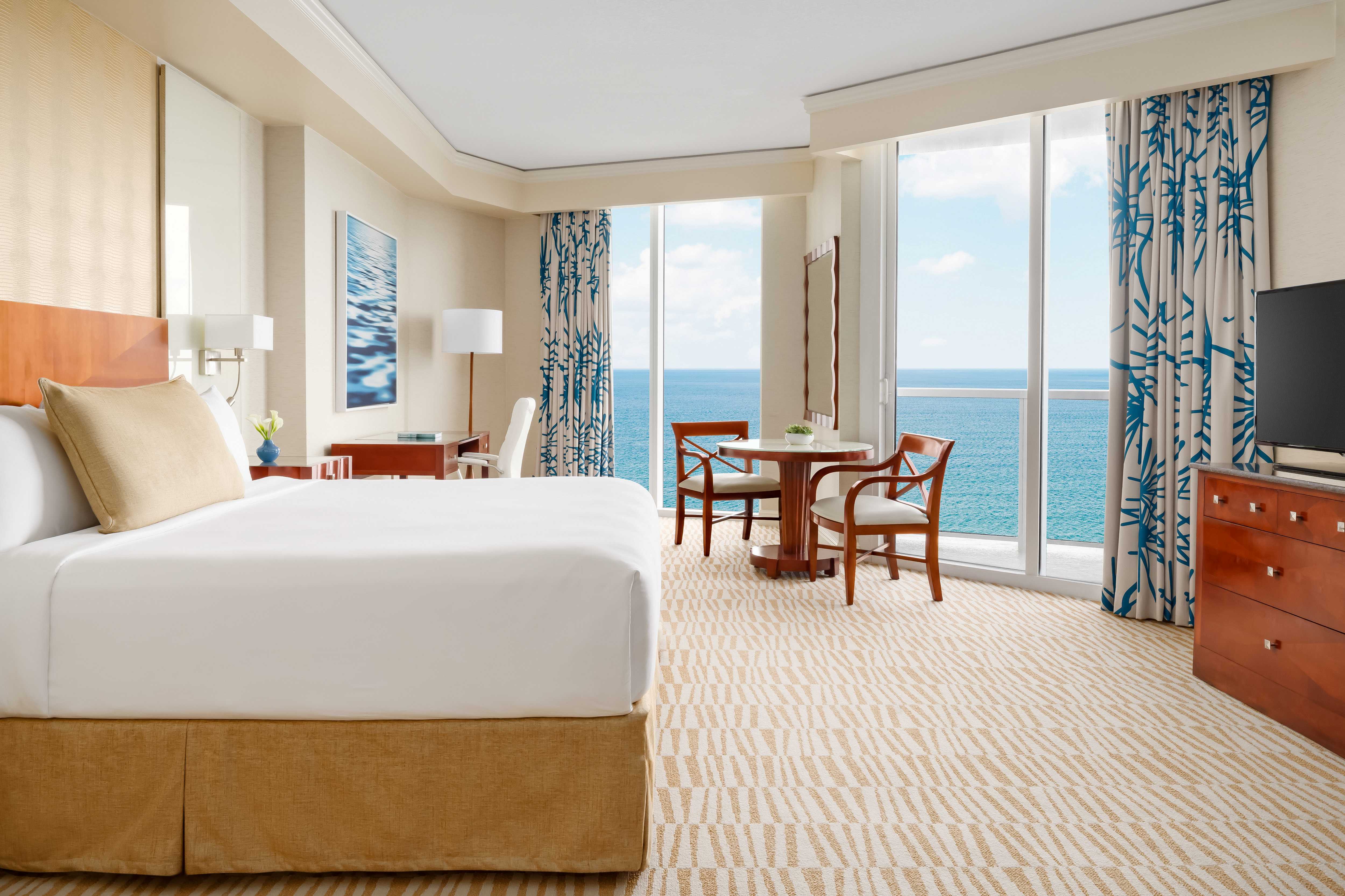 a room with a bed and chairs and a table with chairs and a view of the ocean