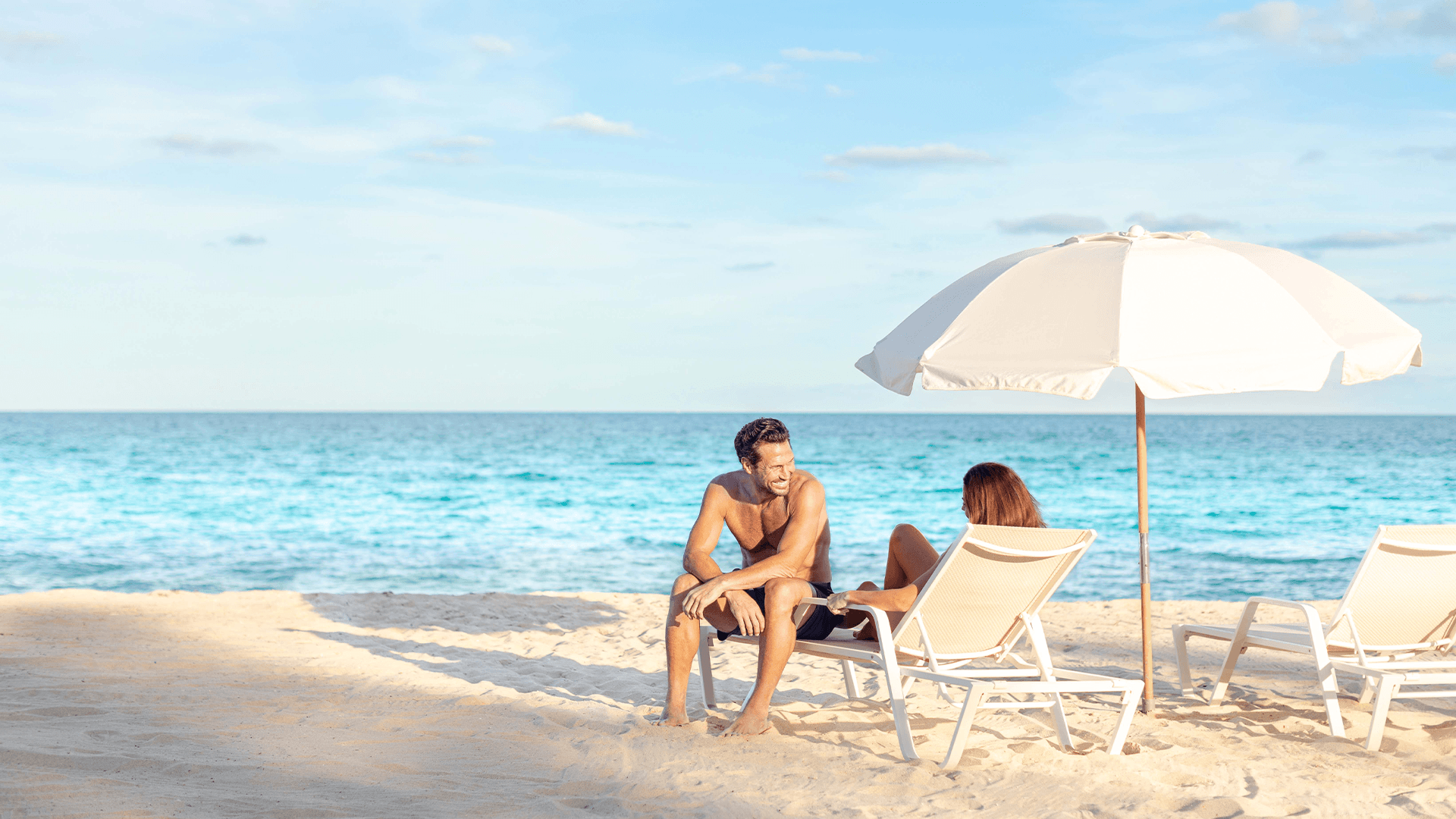 a man and woman sitting on a beach chair under an umbrella