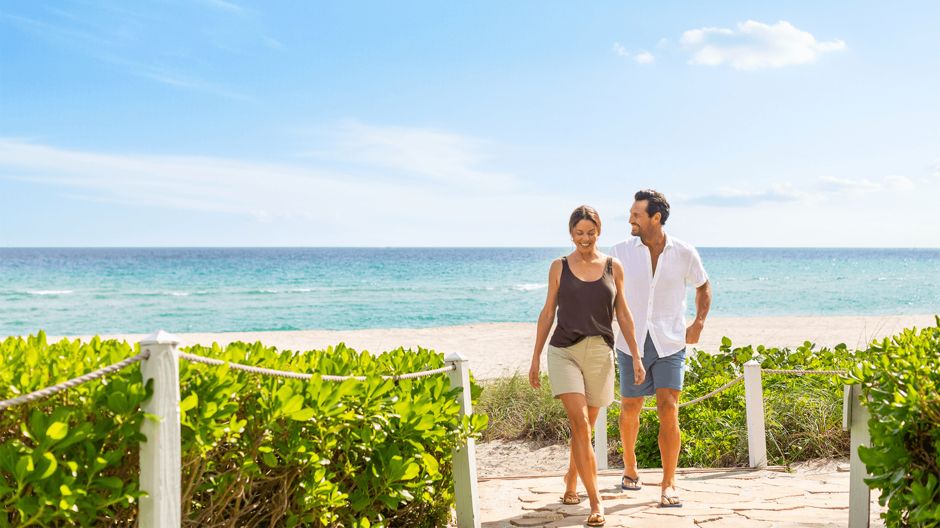 a man and woman walking on a path near a beach