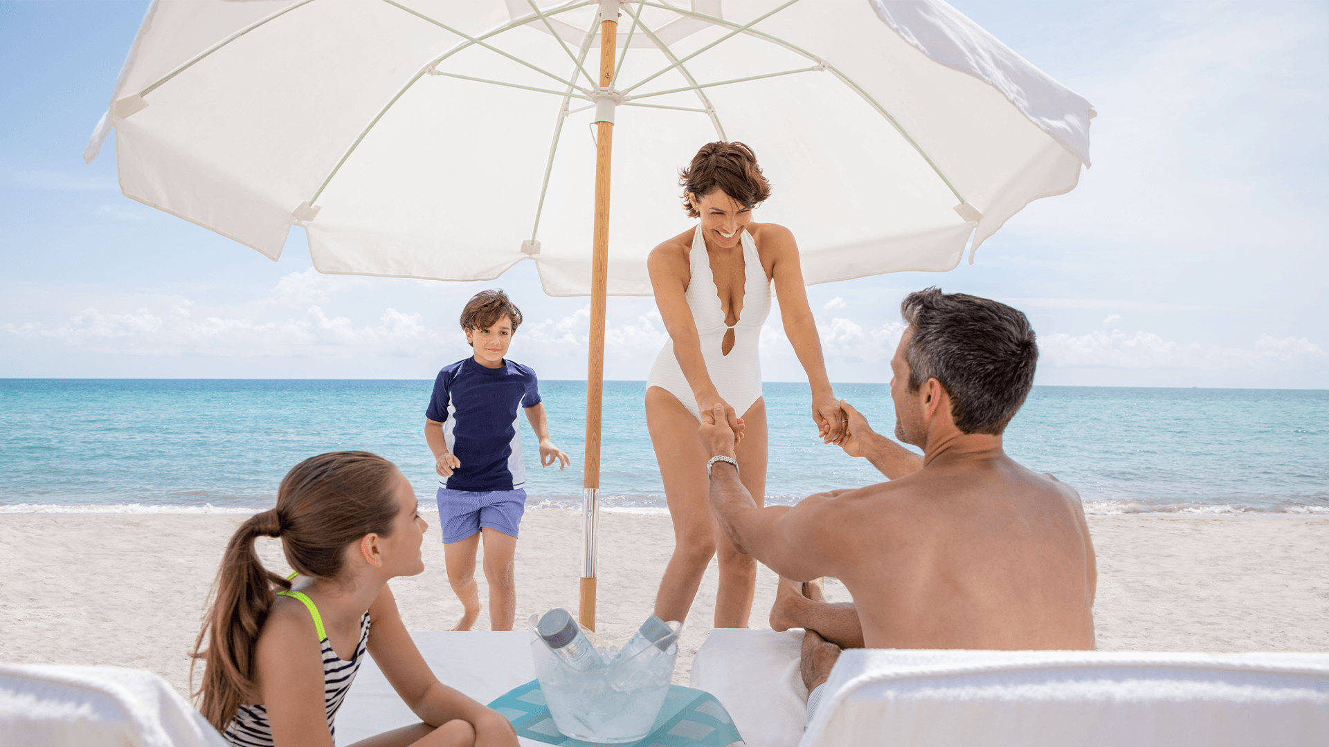 a man and woman holding hands and a woman holding a white umbrella on a beach