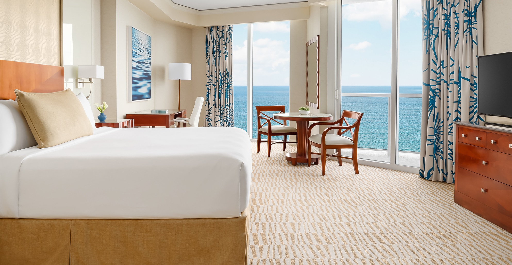 a room with a bed and chairs and a table with a view of the ocean