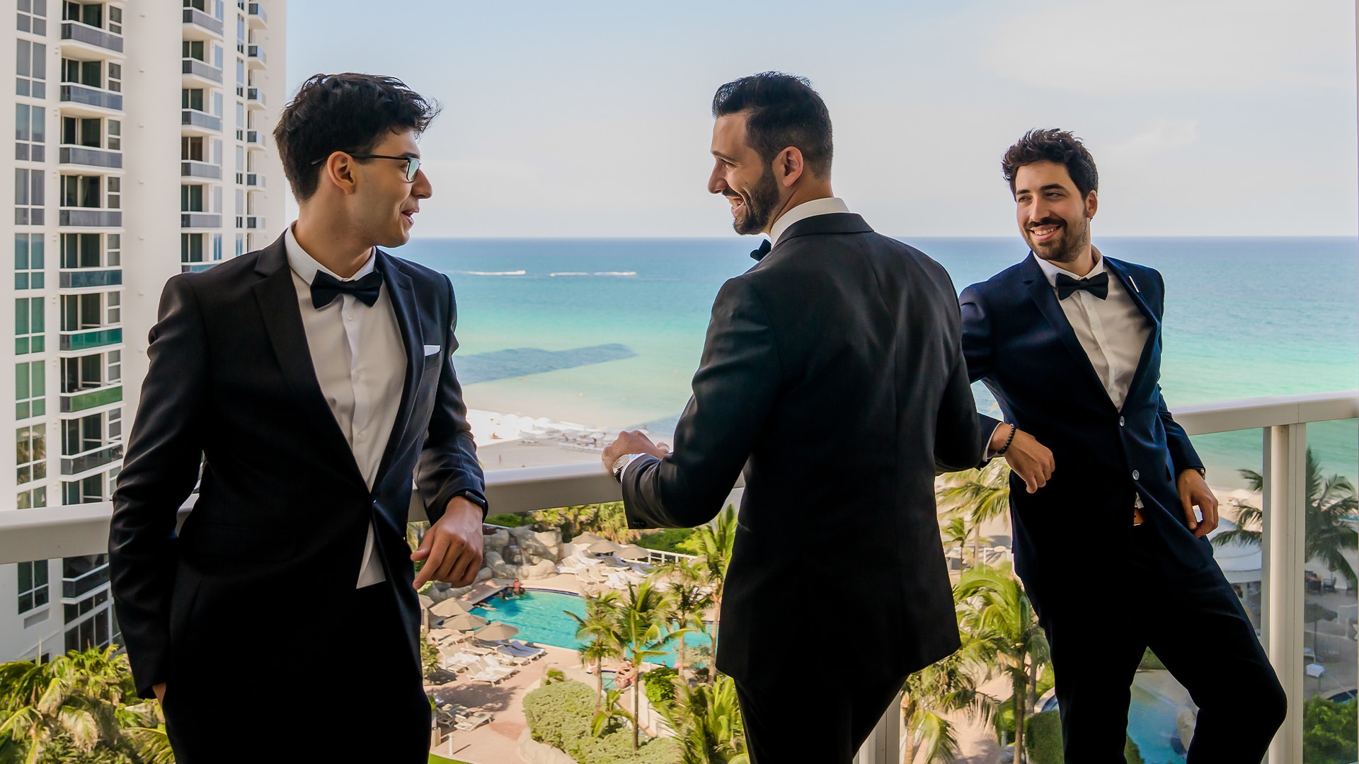 a group of men in suits standing on a balcony overlooking a beach