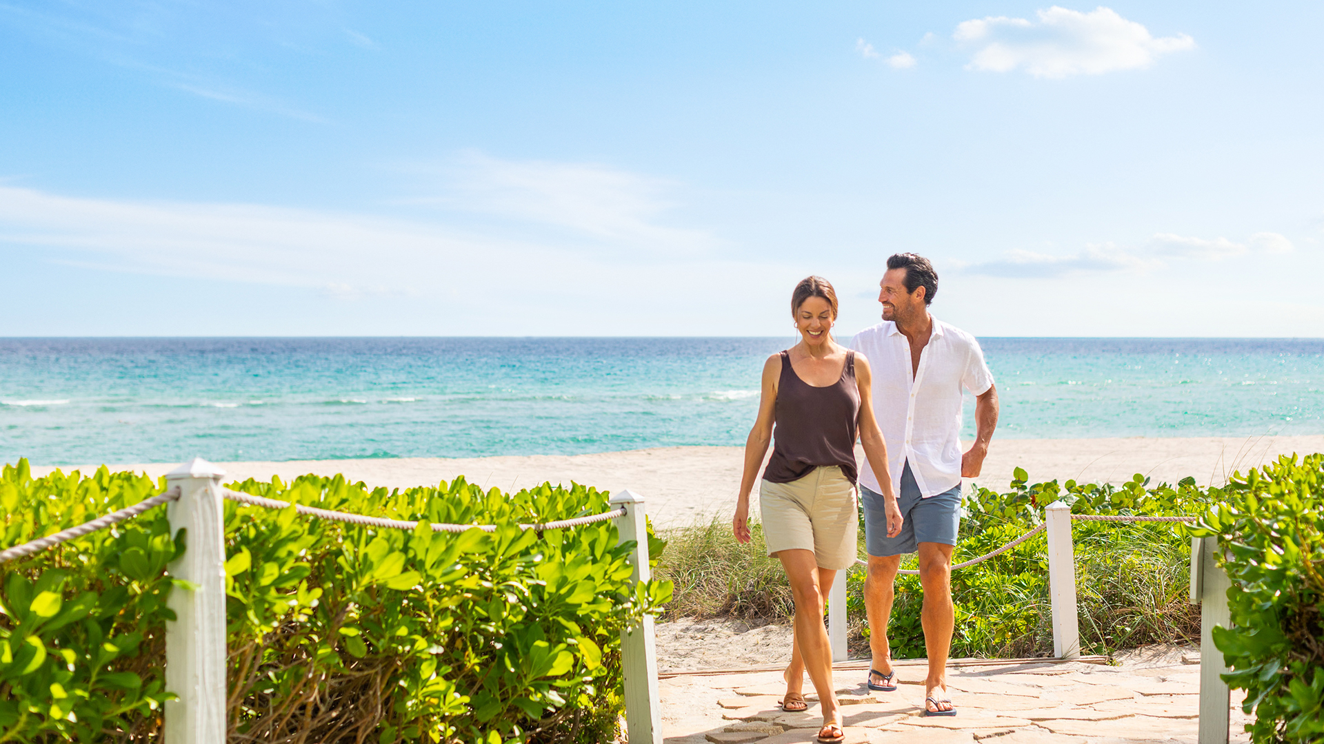 a man and woman walking on a path on a beach
