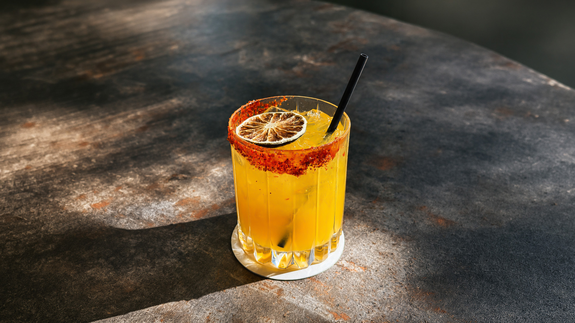 a glass of yellow liquid with a slice of lime and a straw