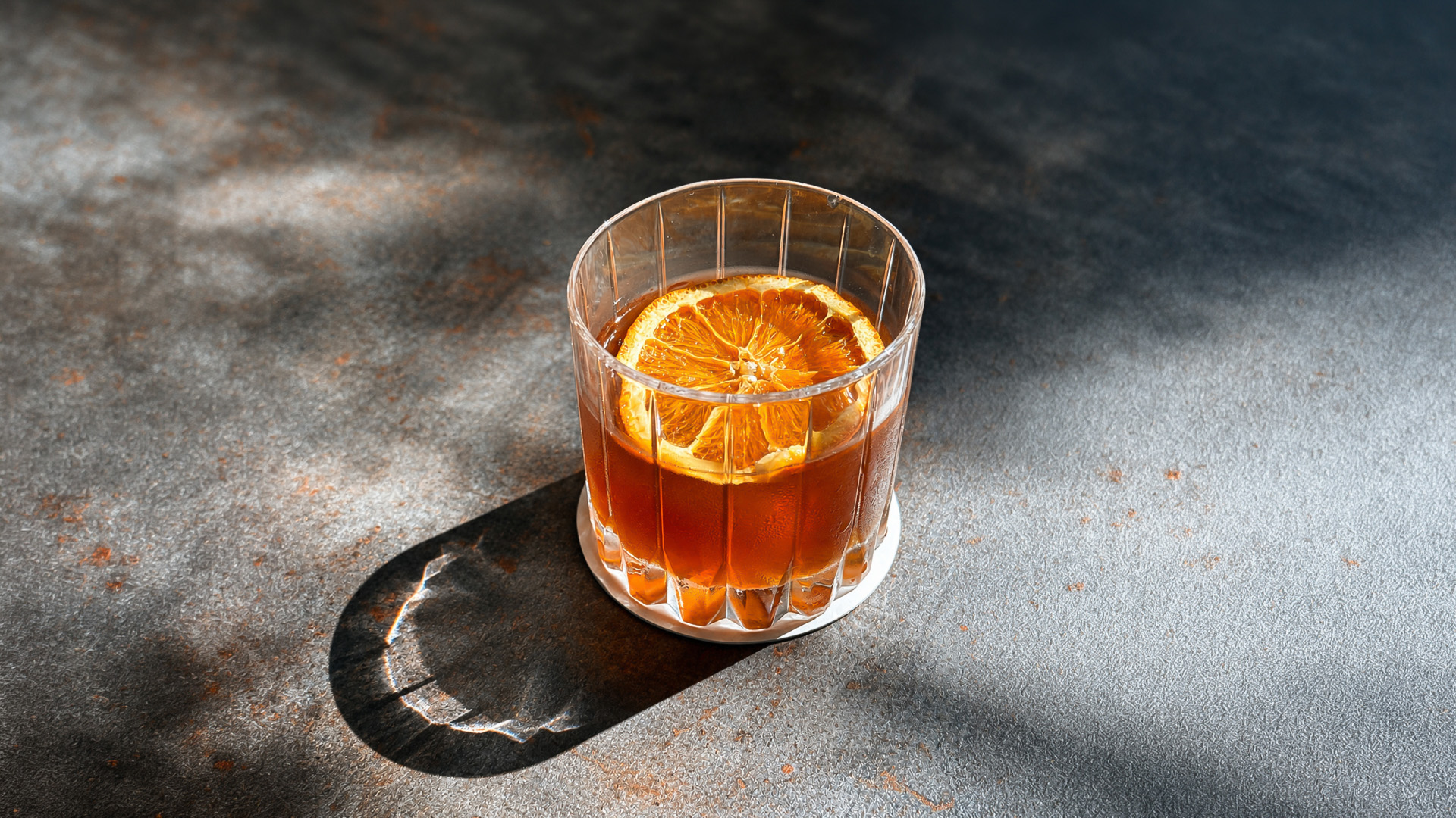 a glass of brown liquid with a slice of orange on a gray surface
