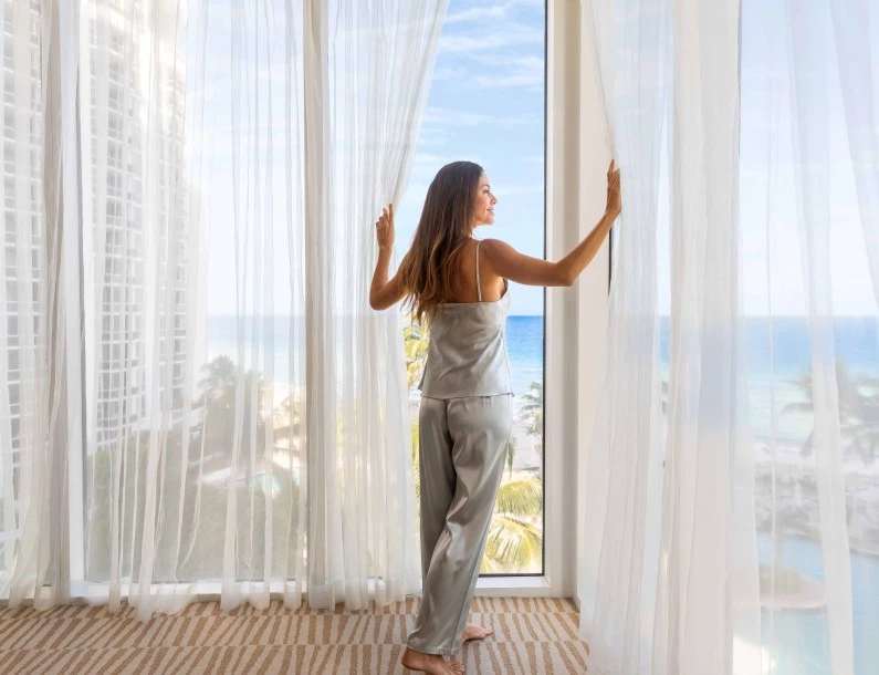 a woman standing in front of a window with a view of the ocean