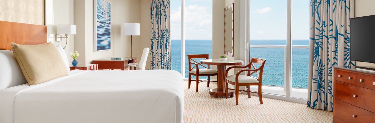 a room with a bed and chairs and a table with chairs and a view of the ocean