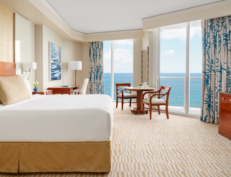 a room with a bed and chairs and a table with chairs and a view of the ocean