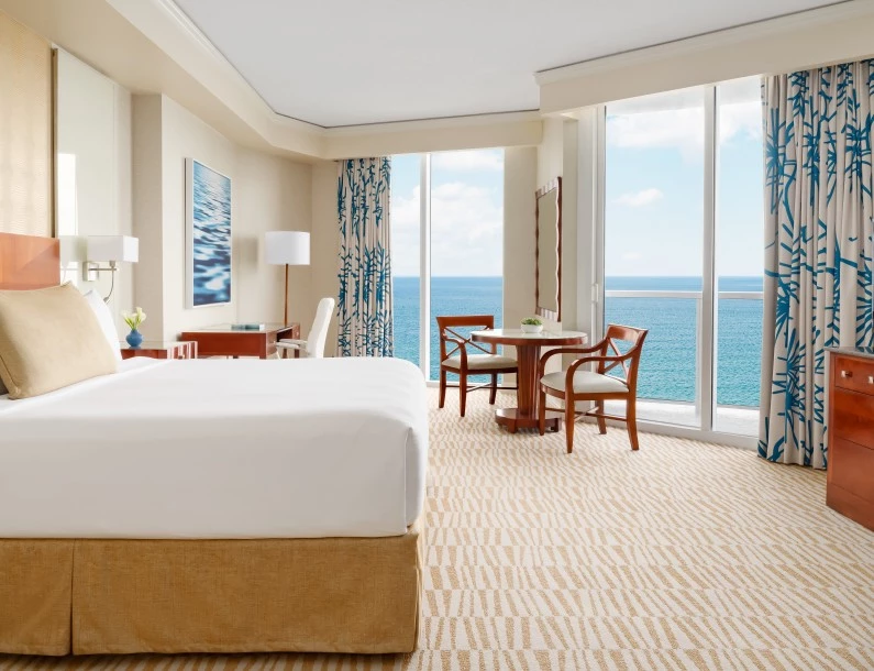 a room with a bed and chairs and a table with chairs and a view of the ocean