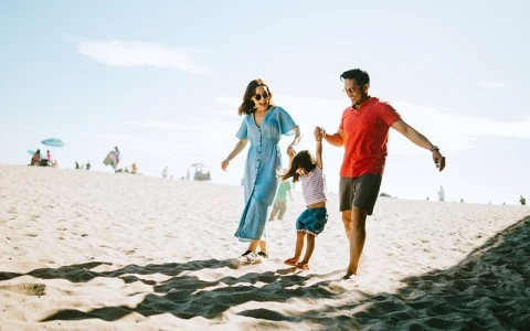 a man and woman holding hands and walking with a child on sand