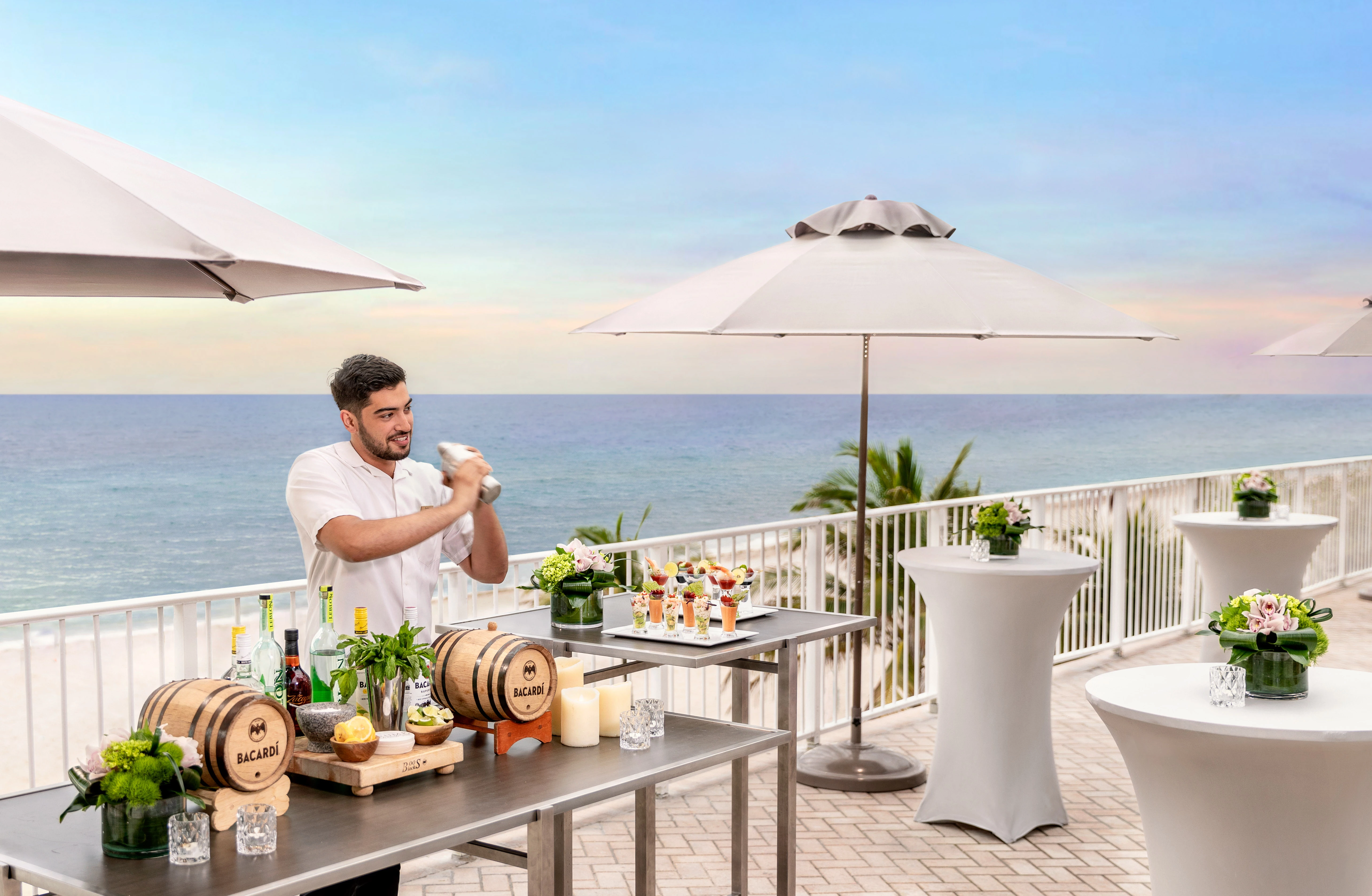a man standing at a table with drinks and umbrellas