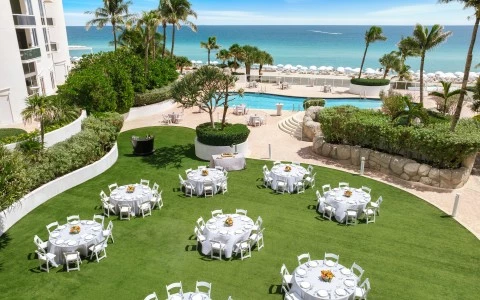 a group of tables and chairs in a lawn with a pool and water in the background