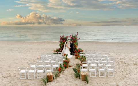 a man and woman standing under a floral arch on a beach