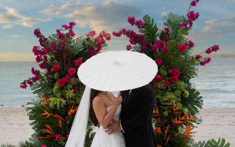 a man and woman in wedding attire under a large white umbrella