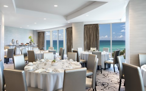 a room with tables and chairs and a view of the ocean