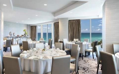a room with tables and chairs and a view of the ocean
