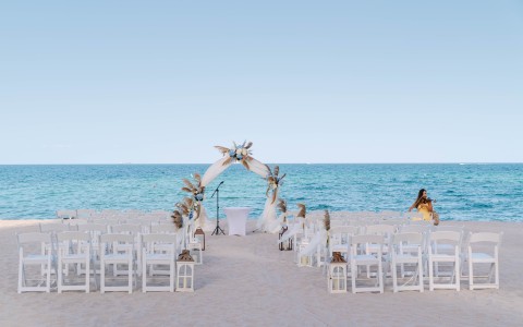 a beach wedding set up with chairs and a woman sitting in the background