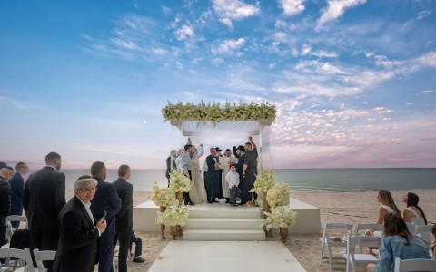 a group of people standing under a wedding ceremony on a beach