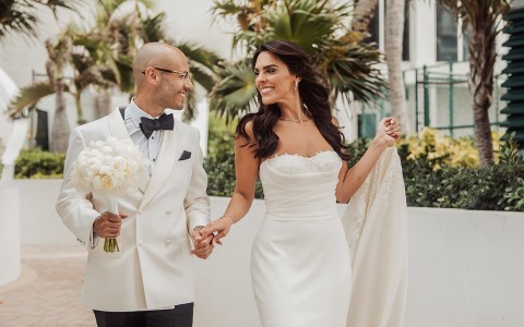 a man and woman in white dress holding hands and walking down a brick path