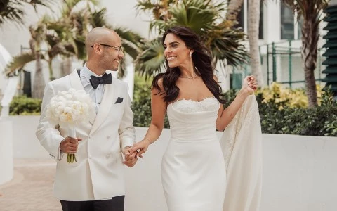 a man and woman in white dress holding hands and walking down a brick path