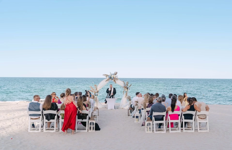 a group of people sitting in chairs at a beach wedding