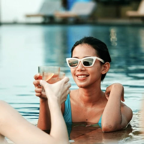 a person in a pool wearing sunglasses and a blue garment holding a glass of water