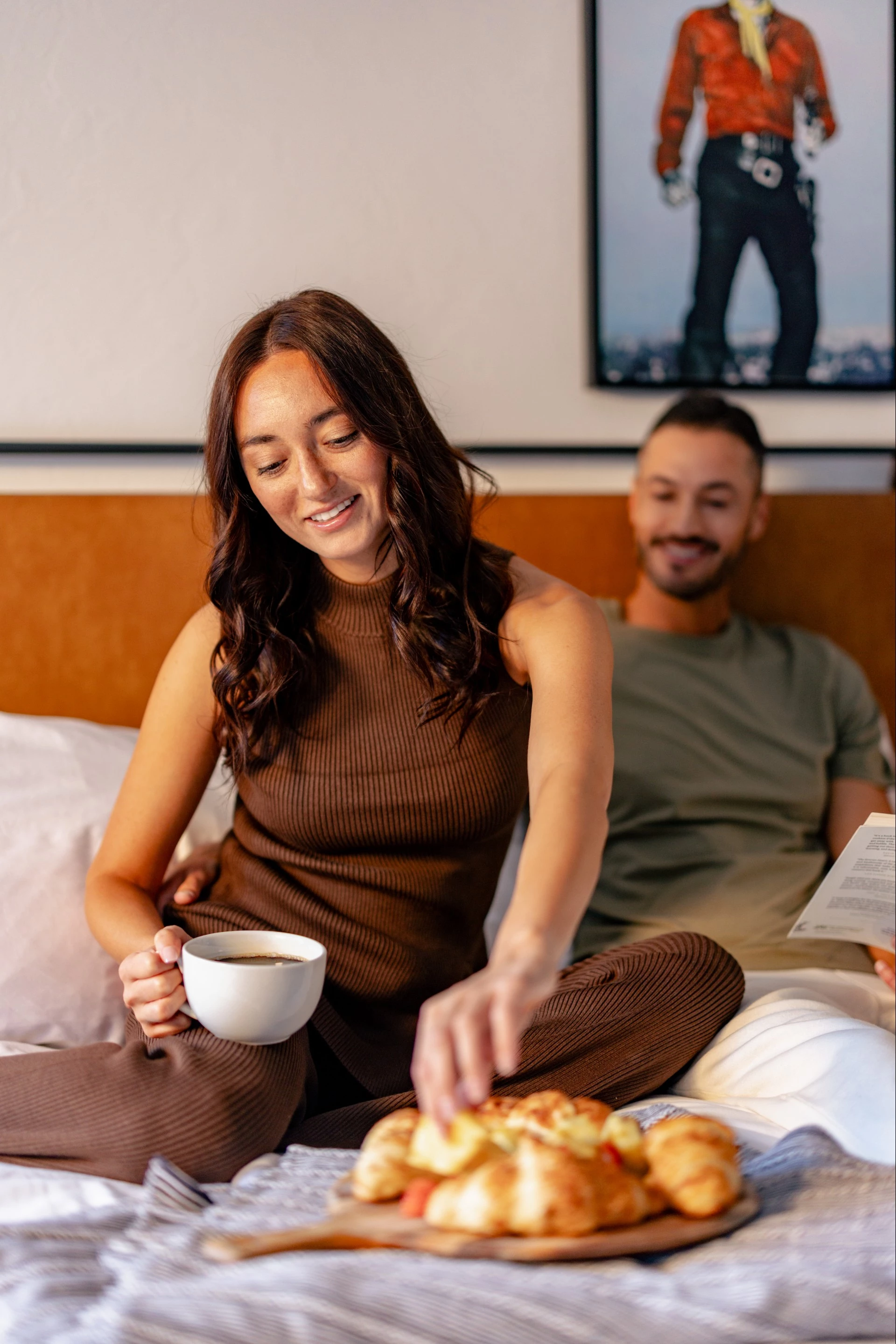 a woman sitting on a bed with a cup of coffee and pizza
