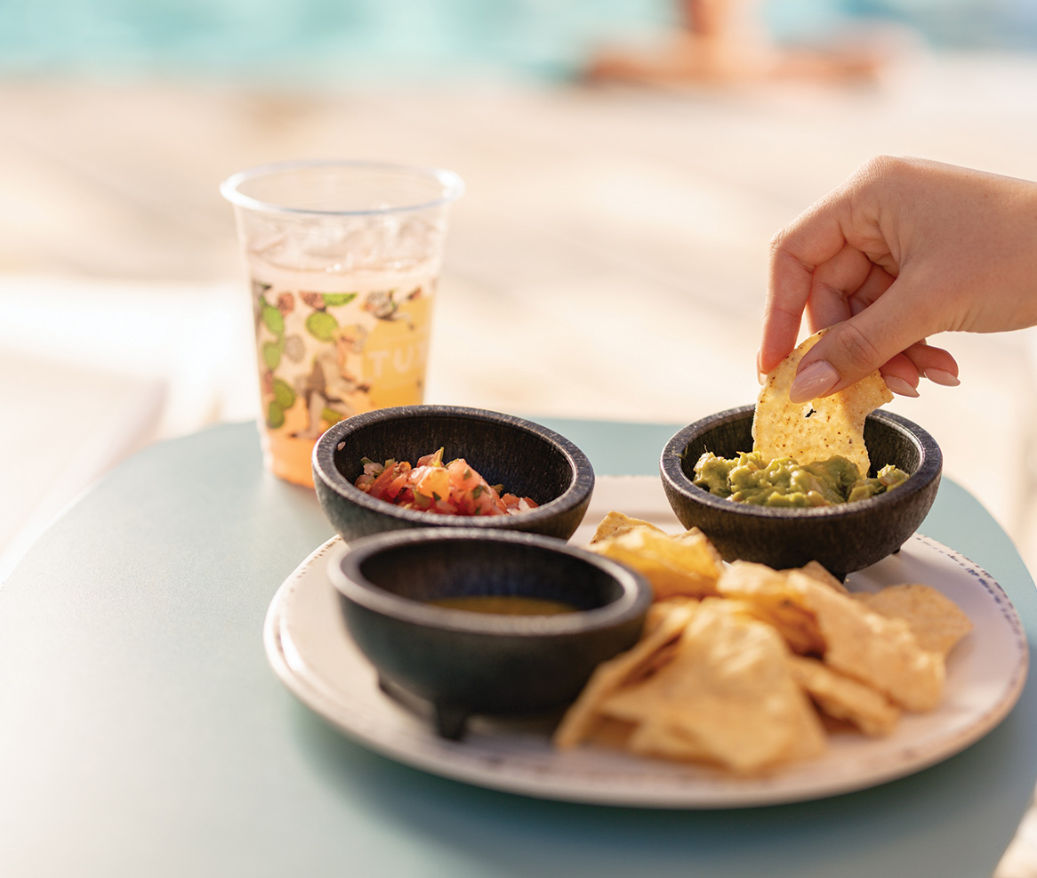a hand dipping a chip into a bowl of salsa