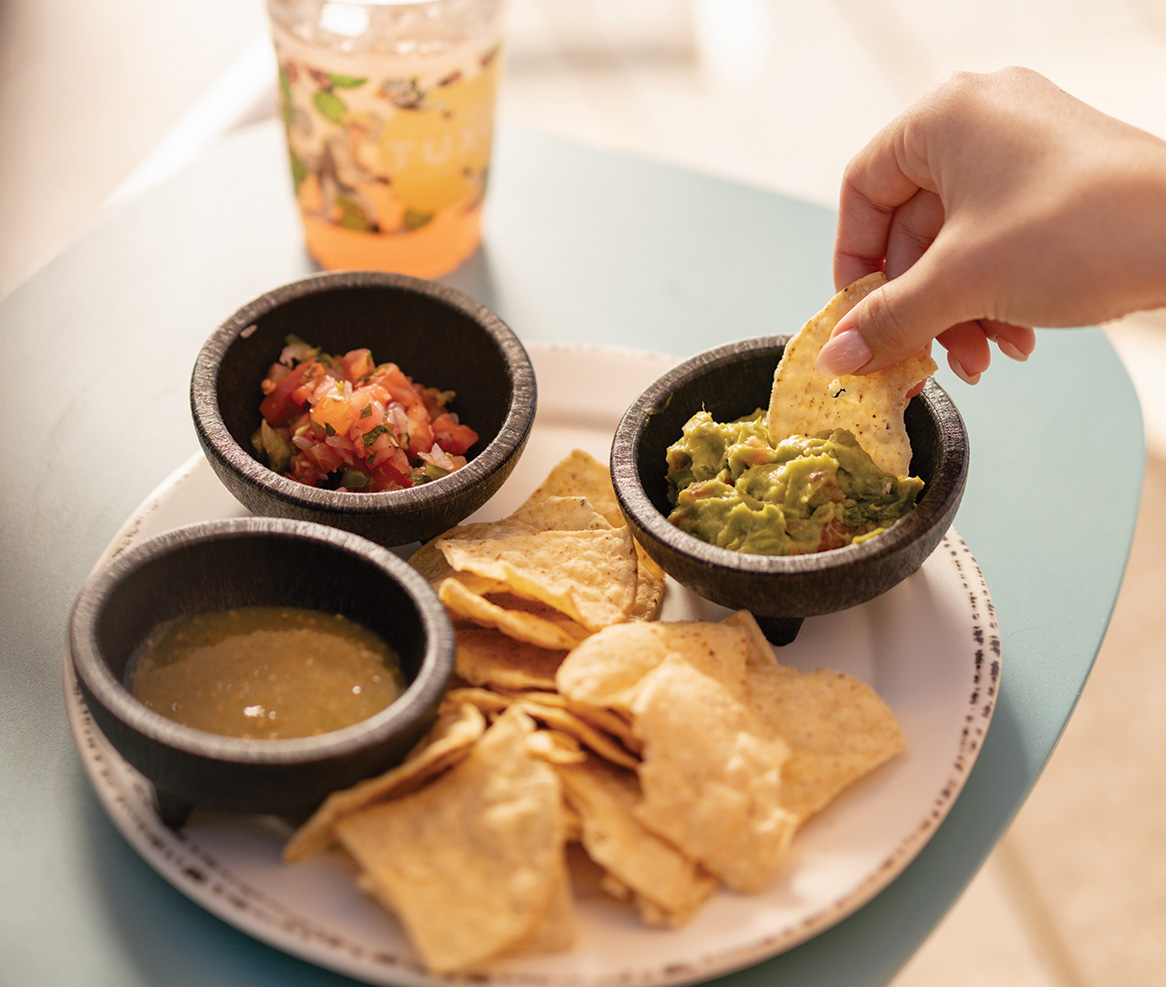 a hand dipping a chip into a bowl of salsa and chips