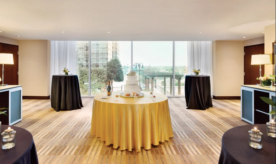 A round table in the center of the room with a cake on it and two taller round cocktail tables in back 