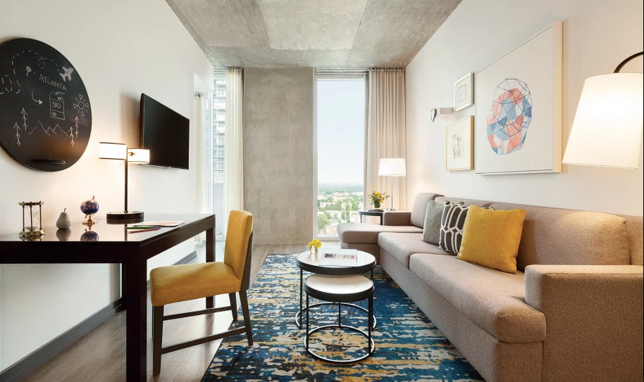 Living room area with desk, cushioned chair, two nesting coffee tables, couch, TV, and decorative pillows, rug, and artwork 