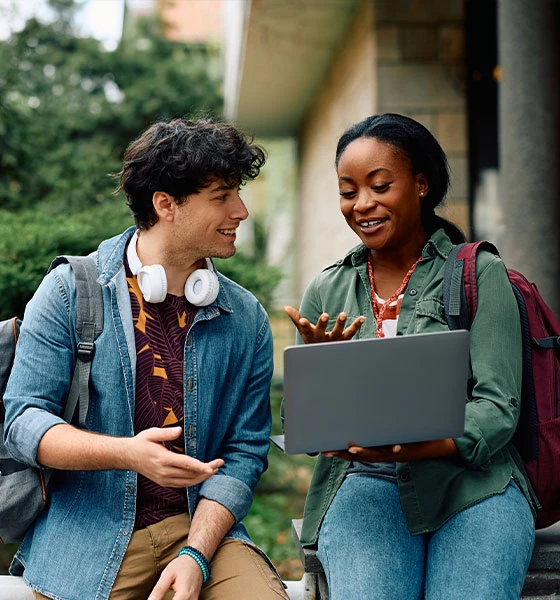 a man and woman sitting on a bench looking at a laptop