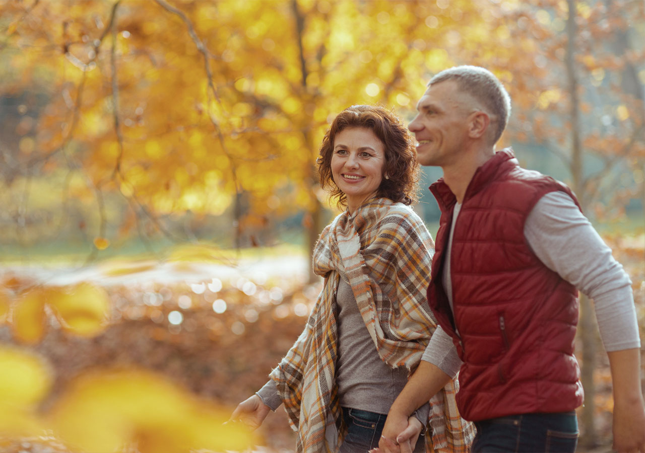 a man and woman holding hands and walking in the woods