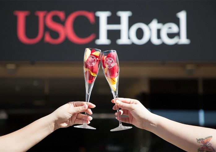 a pair of hands holding wine glasses with flowers in front of a sign