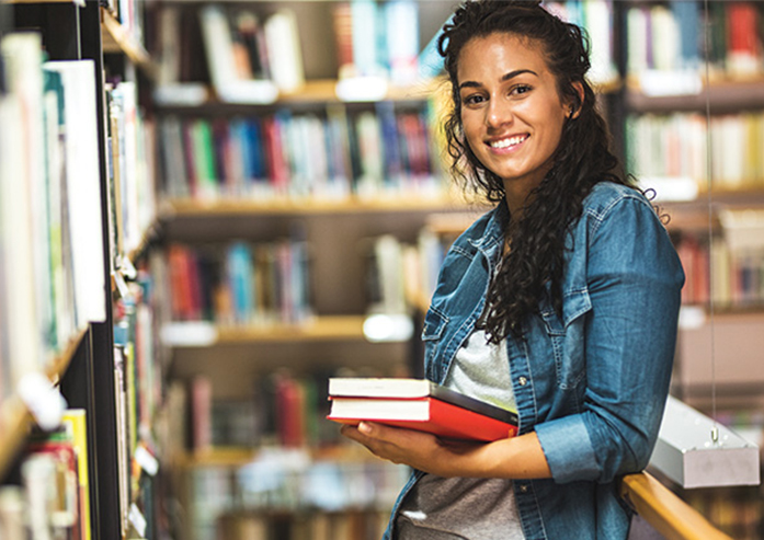 girl in library holding books and smiling