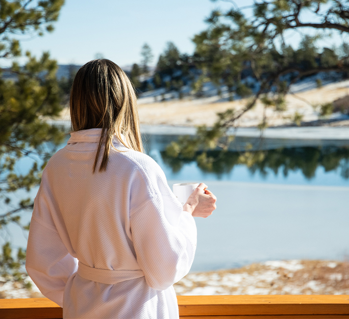 a woman in a white robe holding a cup overlooking a lake