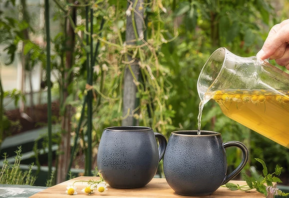 a person pouring yellow liquid into two mugs
