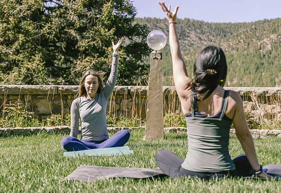 two women sitting on the grass with their hands up