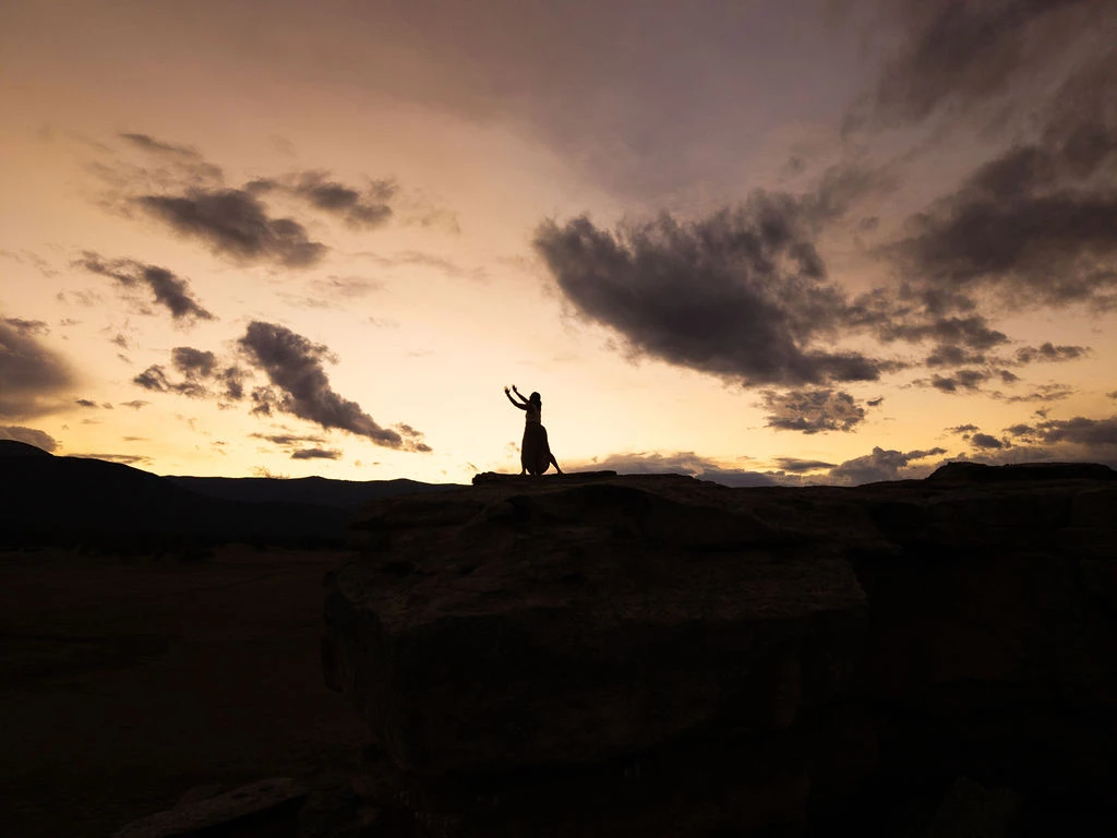 a silhouette of a woman standing on a rock with her arms up