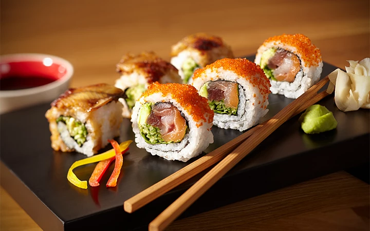 A plate of sushi rolls with chopsticks and wasabi.