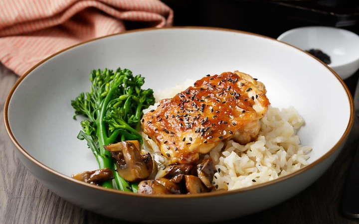 A plated dish of chicken, rice, broccoli, and mushrooms in a white bowl.