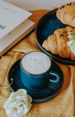 A blue cup of coffee with croissants and flowers on a table
