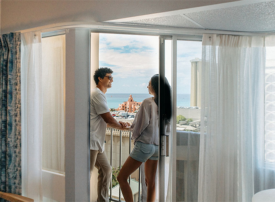 a man and woman standing in a room with a balcony and a view of the ocean