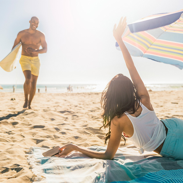 a woman sitting on a beach with a man standing on the beach