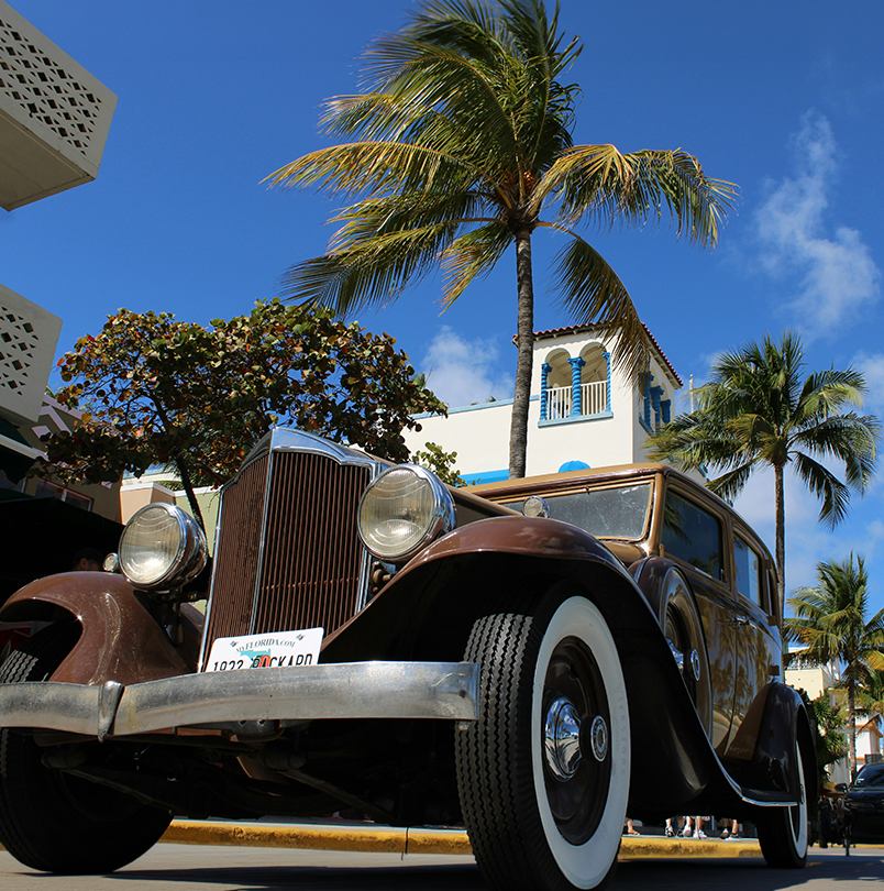 a brown car parked on a street with palm trees and buildings