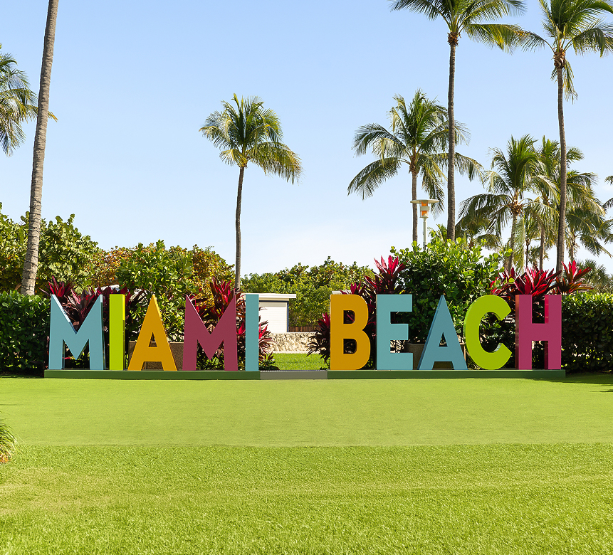 a sign on a lawn with palm trees and bushes